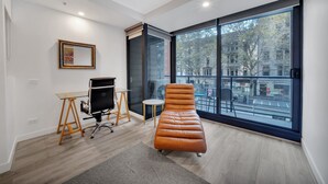 A modern office space with a large window, a desk, a chair, and a cushioned bench. - All on Flinders (Melbourne)