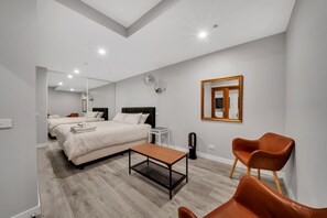 Habitación de hotel moderna con una cama grande, una mesa de madera, dos sillas, una mesita auxiliar y un espejo en la pared.