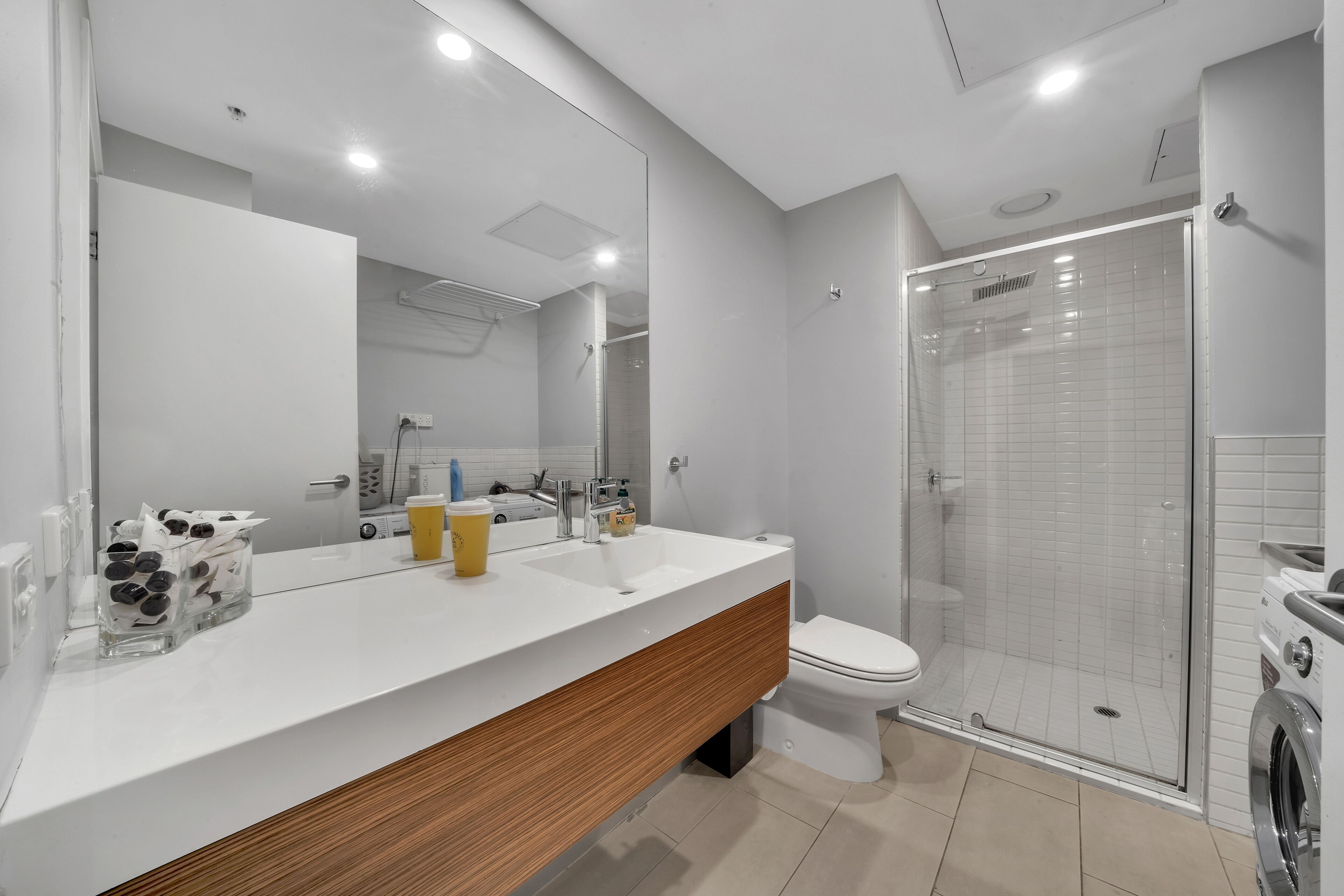 A modern bathroom with a white vanity, a large mirror, a glass shower enclosure, and a toilet.