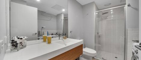 A modern bathroom with a white vanity, a large mirror, a glass shower enclosure, and a toilet.