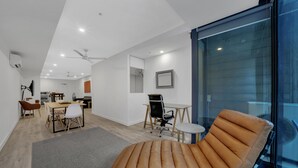 A modern living room with a leather lounge chair, a dining area with a table and chairs, and a kitchen in the background. - All on Flinders (Melbourne)