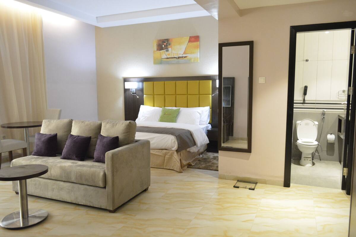 Ein Hotelzimmer mit Bett, einer Couch, einem kleinen Tisch und einem durch eine offene Tür einsehbaren Badezimmer.