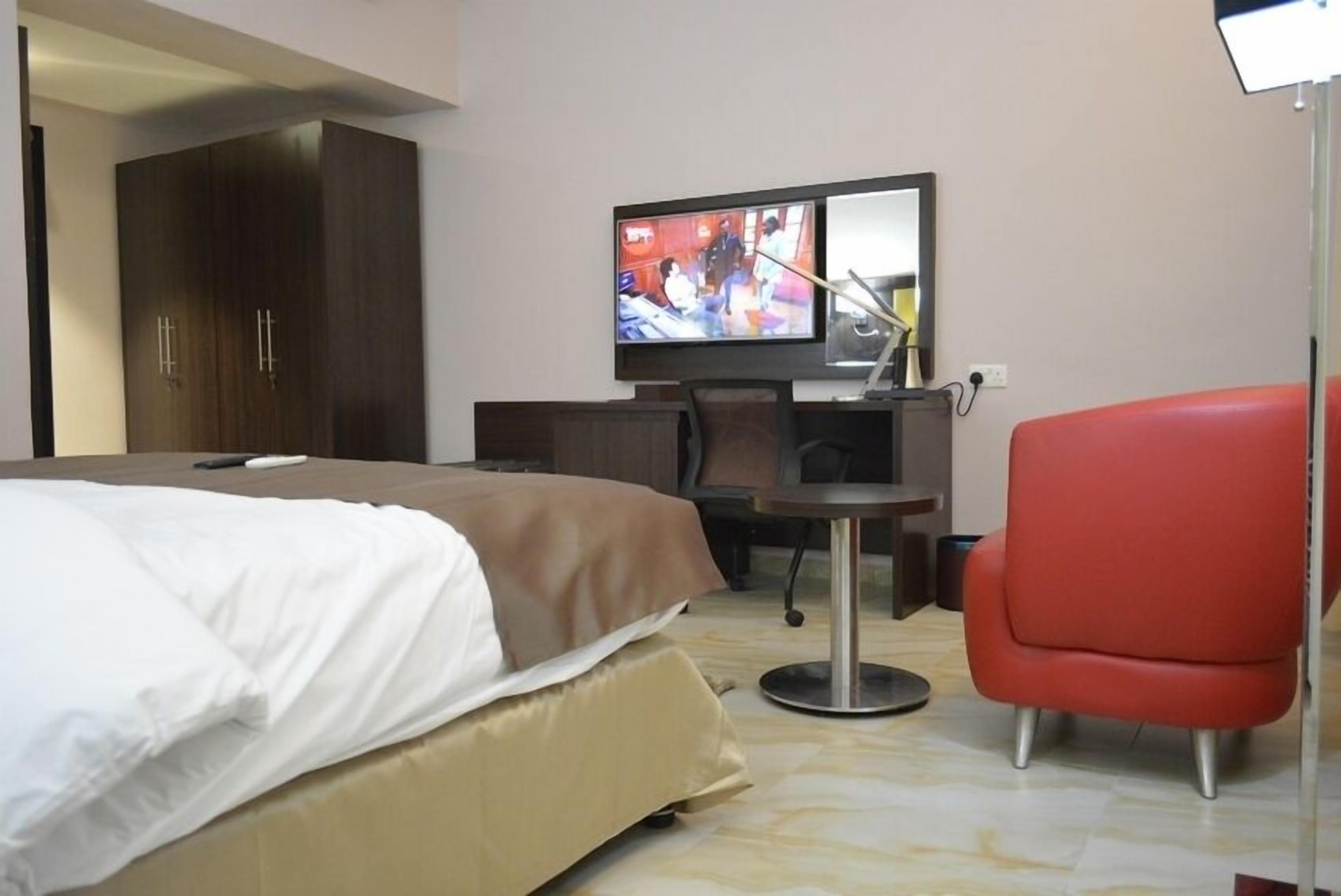 Una camera d'albergo con un letto, una scrivania, una televisione e una poltrona rossa.