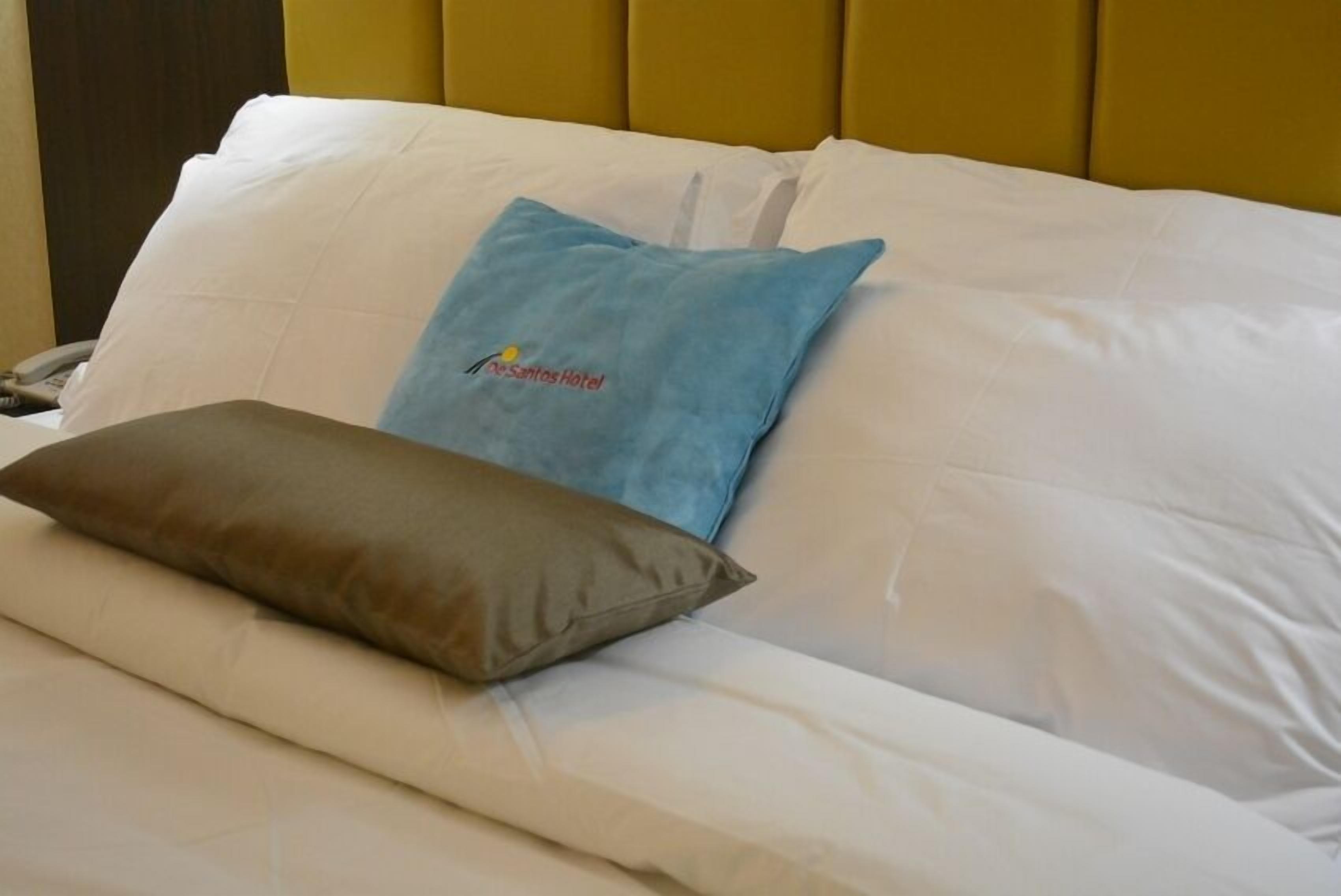 Una cama con ropa blanca, una almohada azul con un logotipo y una almohada marrón.