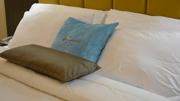 Una cama con ropa blanca, una almohada azul con un logotipo y una almohada marrón.