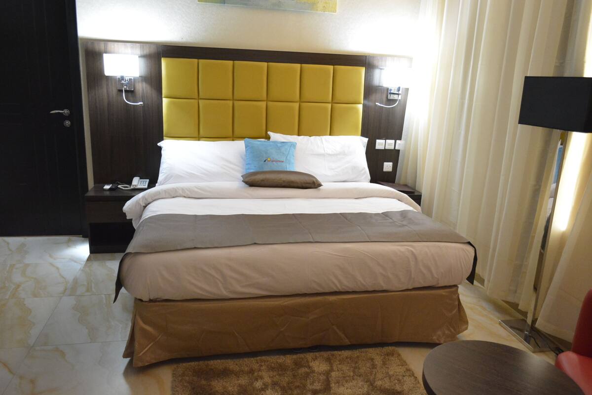 Ein Hotelzimmer mit einem großen Bett, einem Nachttisch mit Lampe und einem Beistelltisch mit Telefon.