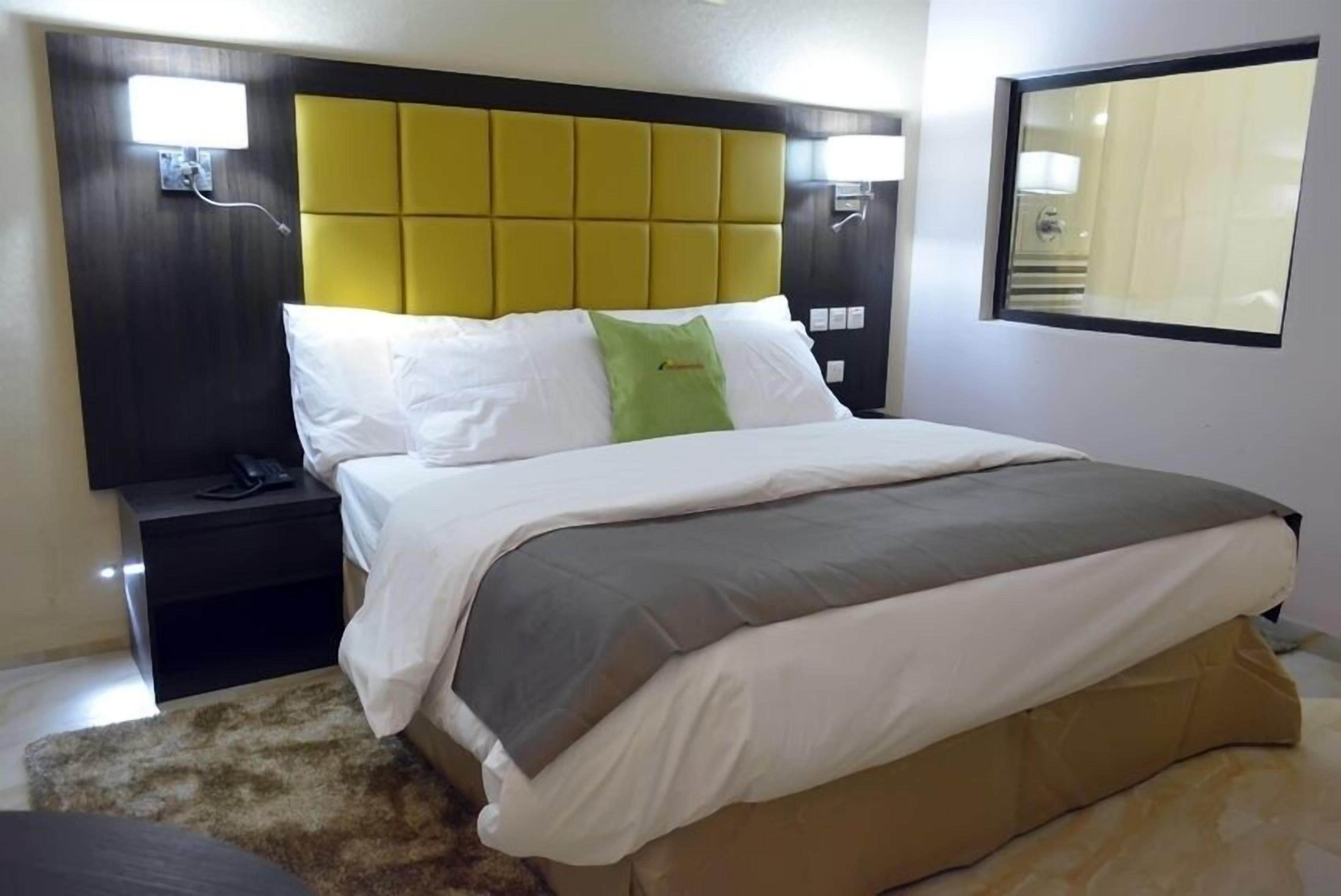 A hotel room with a bed, a nightstand, a lamp, and a window.