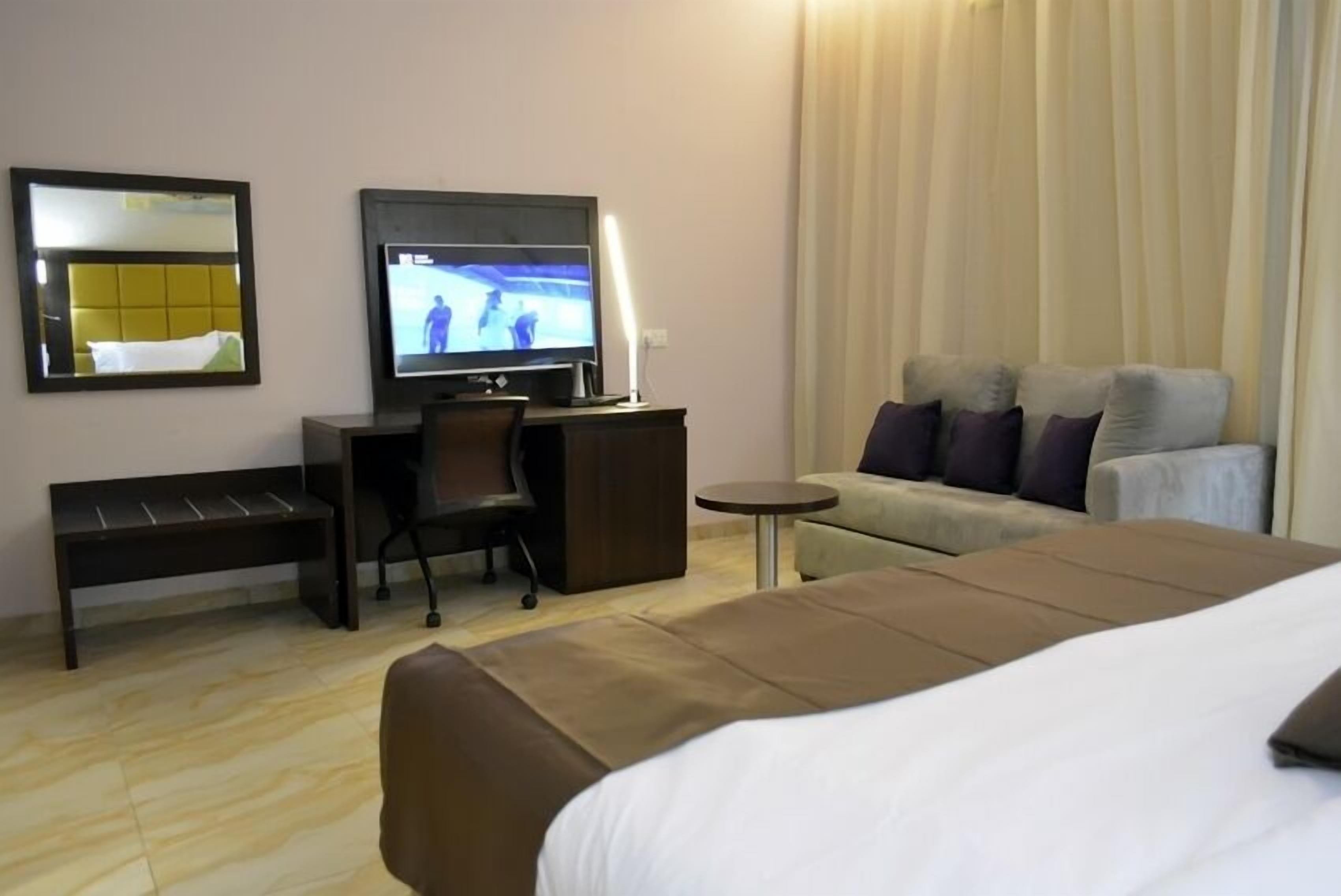 A hotel room with a bed, a desk with a computer, a chair, a small table, and a sofa.