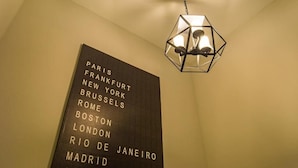 A wall with a list of city names in uppercase letters, a geometric hanging light fixture above it, and a chain connecting the fixture to the ceiling. - The Rich Sotel (Krabi)