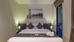 A hotel room with a neatly made bed, two bedside tables with lamps, a cityscape artwork on the wall, and a window with curtains. - The Rich Sotel (Krabi)