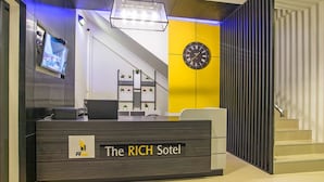 A reception desk with a clock, a TV, and a staircase in the background. - The Rich Sotel (Krabi)