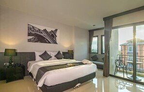 A modern hotel room with a large bed, two bedside tables, a nightstand, a balcony with a chair, and a cityscape view. - The Rich Sotel (Krabi)