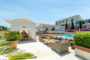 A poolside area with lounge chairs, a wooden table, and a covered seating area with a white canopy. - Antmare Hotel (Cesme)