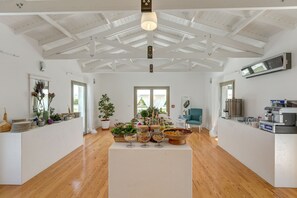 A spacious room with a high ceiling, wooden beams, a central island with food and drinks, a large window, and a seating area with a blue chair. - Antmare Hotel (Cesme)