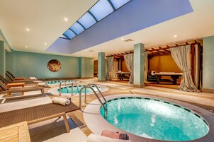 Uma área de piscina interna com várias piscinas, espreguiçadeiras e um claraboia no teto.
