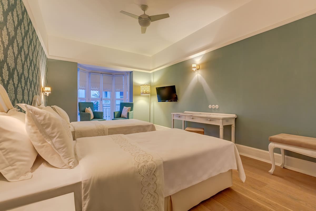 A bedroom with two beds, a desk, a chair, a TV, and a ceiling fan.