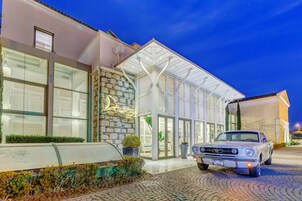 Un hotel con fachada de piedra, amplias ventanas y un coche clásico estacionado al frente.