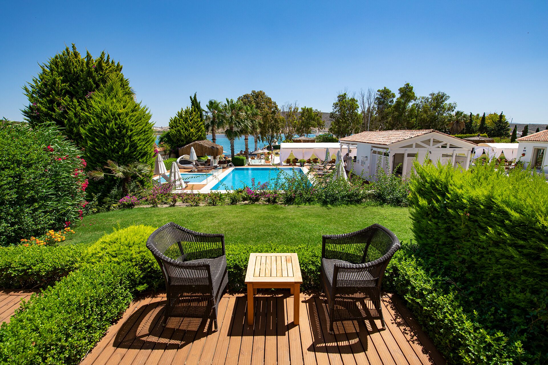 Un espace piscine avec des chaises longues et une table, entouré de verdure et sous un ciel dégagé.