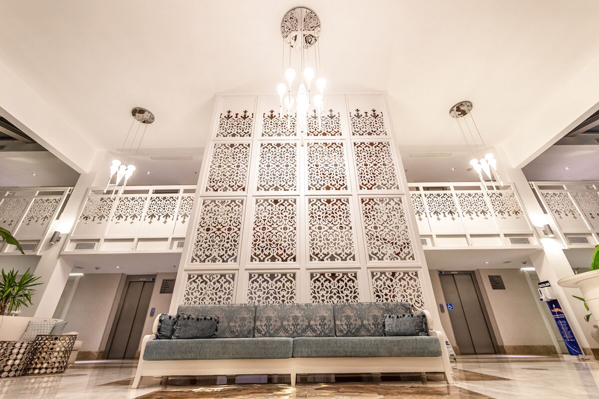 A lobby with a central seating area, a decorative wall with intricate patterns, and a chandelier.