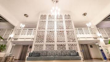 A lobby with a central seating area, a decorative wall with intricate patterns, and a chandelier.