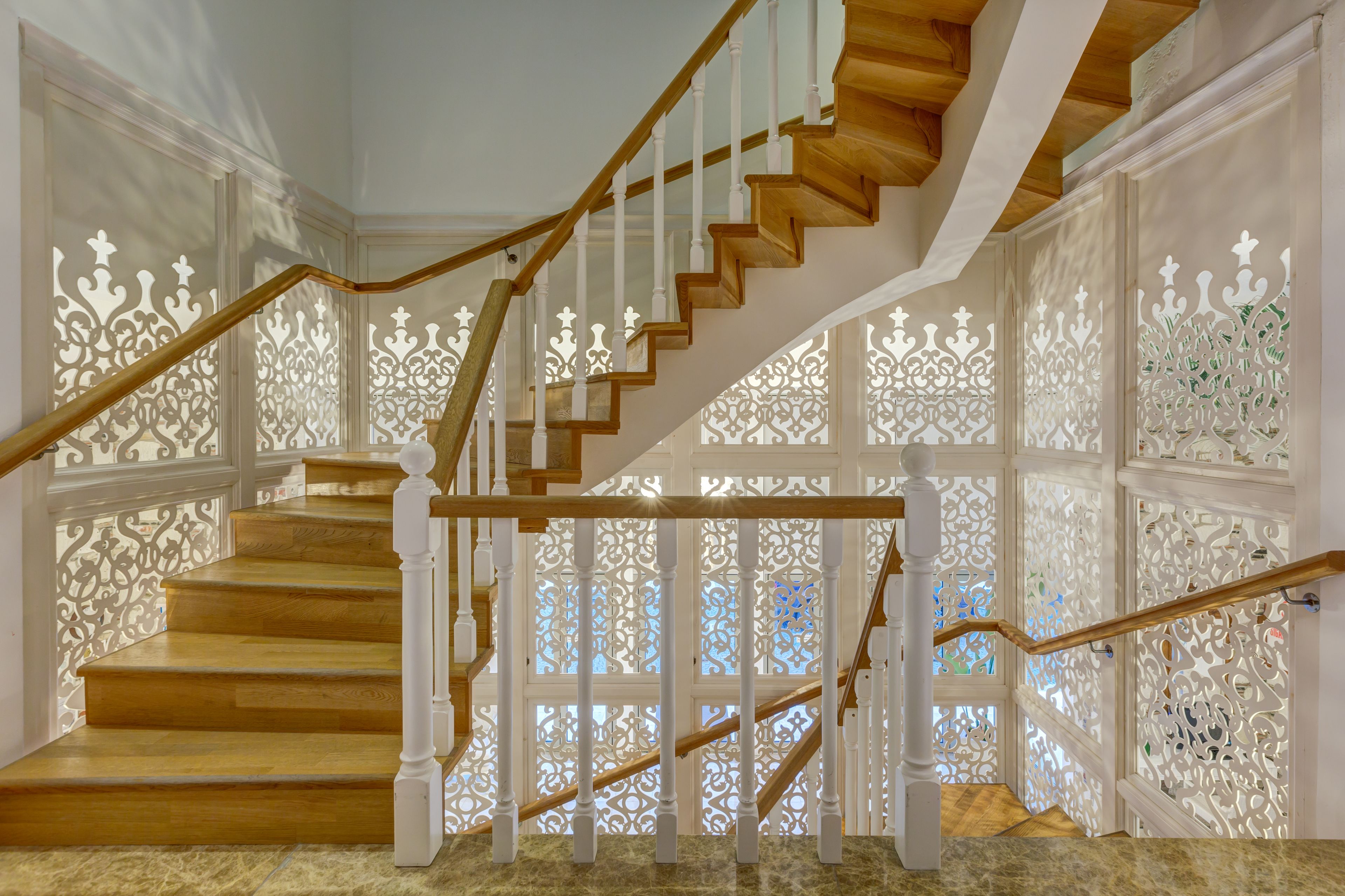 Una escalera de madera con barandillas blancas y paneles de vidrio decorativos.