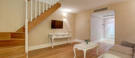 A living room with a wooden staircase, a white console table, a white coffee table, and a beige sofa.
