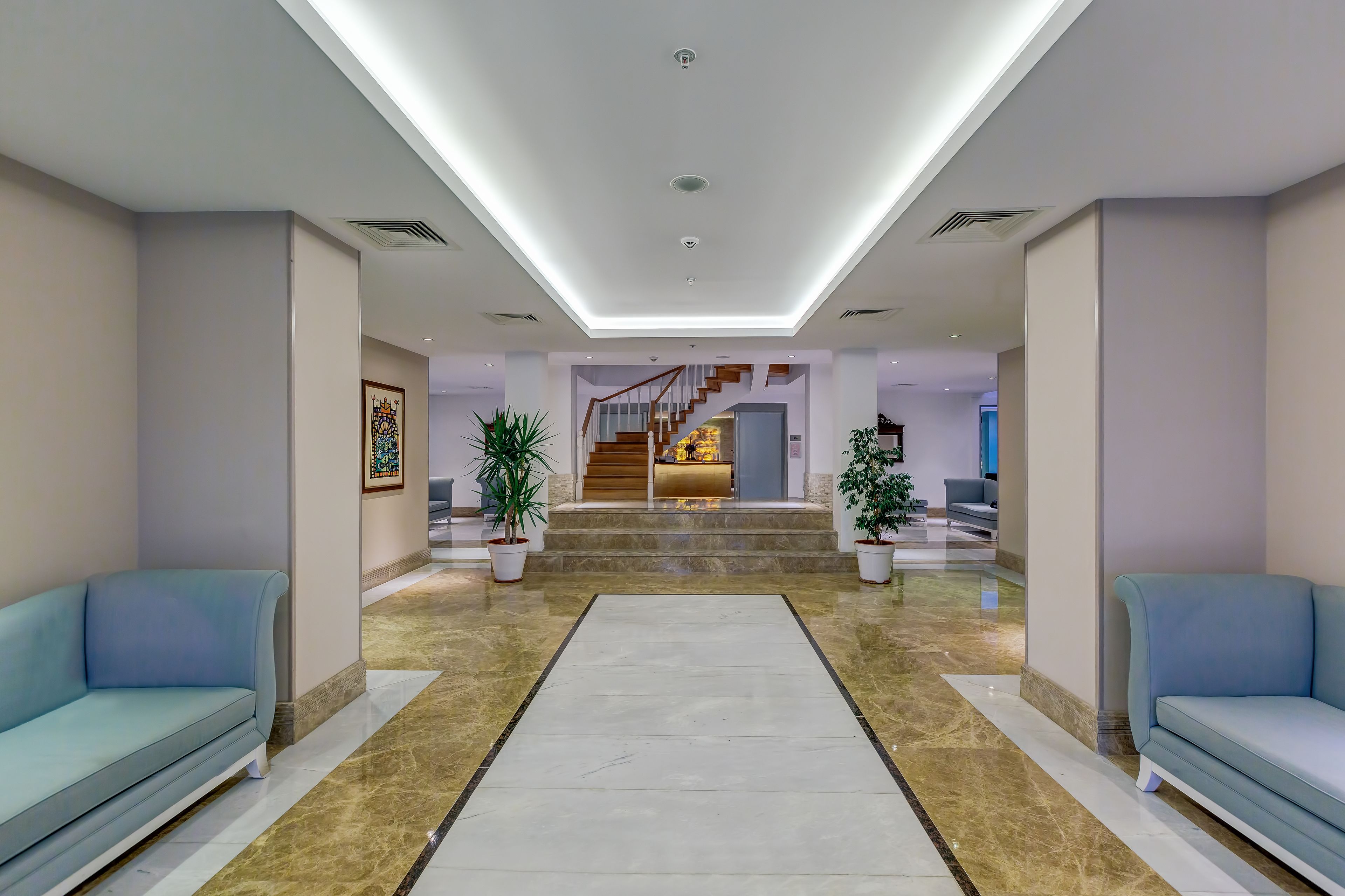 En moderne lobby med en central trappe, lyseblå sofaer og potteplanter.