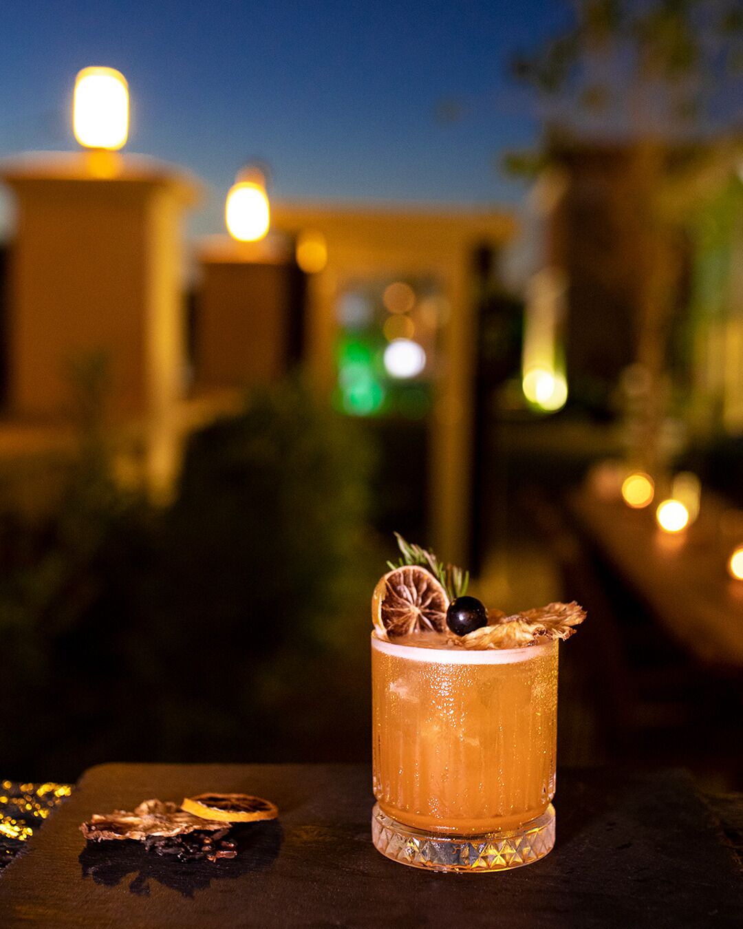 A cocktail with a garnish on a table with candles in the background.