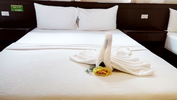 Ein ordentlich gemachtes Bett mit weißen Leinen und einem in Schwanform drapierten Handtuch, eine gelbe Rose und ein grünes Schild am Kopfteil.