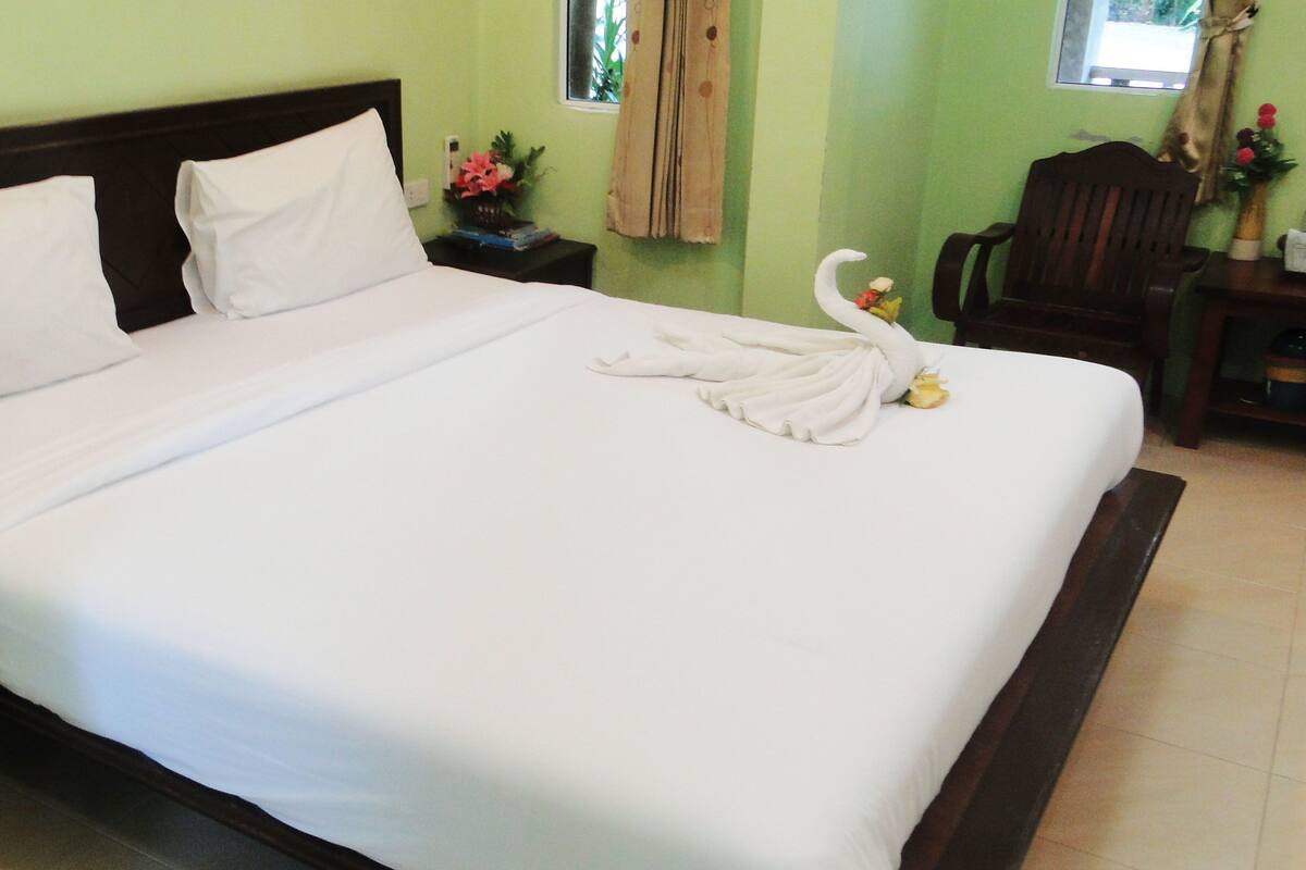 Una cama bien hecha con sábanas blancas, cabecera de madera y almohada decorativa con forma de cisne.