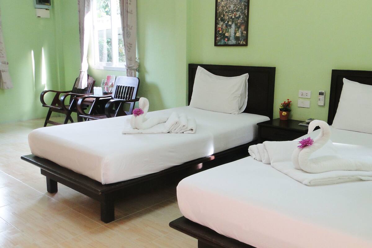 Habitación de hotel con dos camas, cada una con ropa blanca y toallas decoradas con forma de cisne. Cuenta con una pequeña mesa con sillas y una ventana con cortinas.