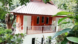 Ein kleines, eingeschossiges Haus mit rotem Dach und weißen Wänden, umgeben von üppiger Vegetation.