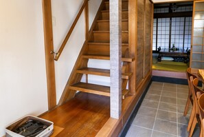 A wooden staircase with a stone pillar, leading to a traditional Japanese room with tatami flooring and a low table with chairs. - KumoMachiya Nijojo (Kyoto)