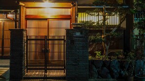 Uma casa japonesa tradicional com um portão deslizante, um acesso coberto e um pequeno jardim com pedras e plantas.