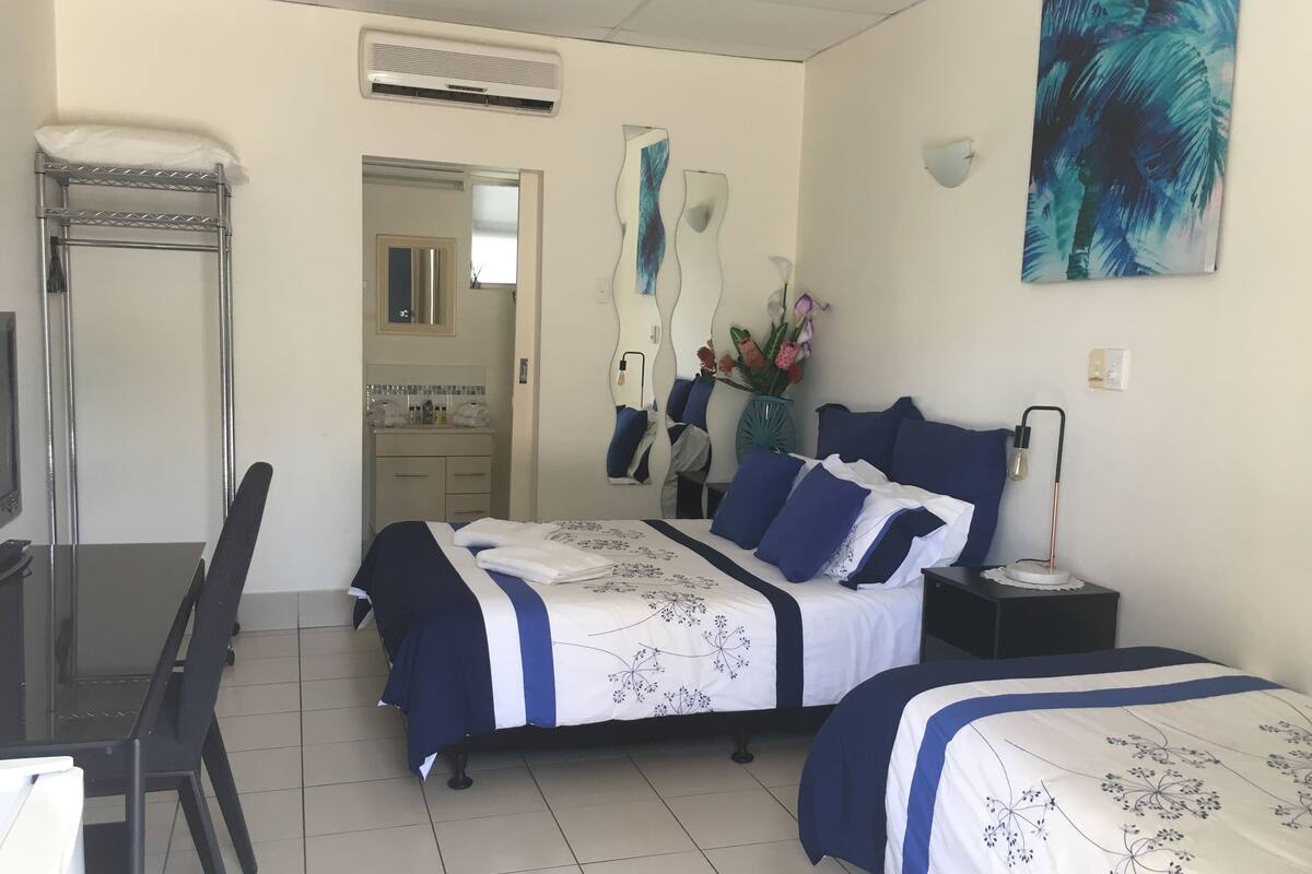 A hotel room with a bed, bedside table, chair, and a bathroom visible through an open door.