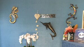 Un área de recepción con pared azul, un letrero de bienvenida, una decoración de delfín, una decoración de lagarto y una mesa con orquídeas blancas.