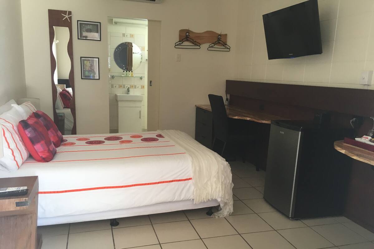 A hotel room with a bed, a desk, a chair, a TV, and a minibar.