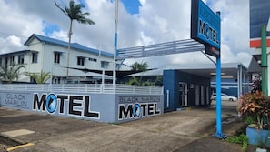 A motel with a prominent sign, a covered parking area, and a building with a blue roof. - Black Marlin Motel (Innisfail)