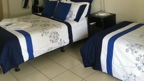 Habitación de hotel con dos camas, una mesita de noche, un espejo en la pared, un cuadro y un florero con flores.