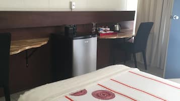 Ein Hotelzimmer mit Bett, Schreibtisch, Fernseher, kleinem Kühlschrank und einer Tür.