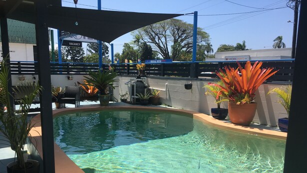 Una piscina cristalina con una estructura de sombrilla, plantas en macetas y una vista de un puente y edificios al fondo.