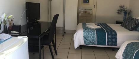 A hotel room with a desk, chair, bed, and a small bathroom.