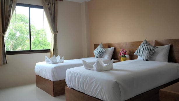 Une chambre d’hôtel avec deux lits, chacun agrémenté de draps blancs et de coussins décoratifs. Il y a une fenêtre avec des rideaux, ainsi qu’une petite table sur laquelle est posé un vase de fleurs.