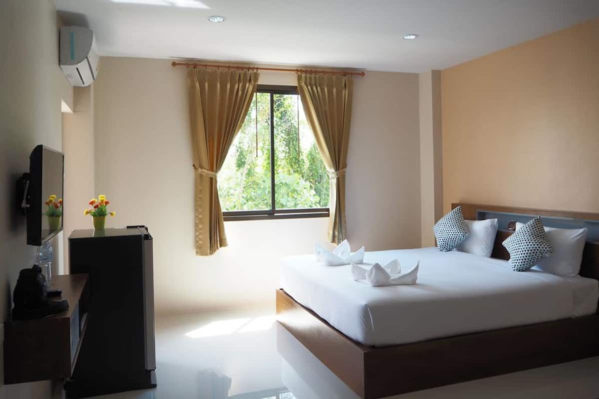 A bedroom with a large bed, a TV, a desk, and a window with curtains.