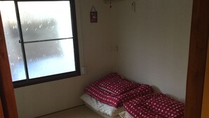 Ein kleiner Raum mit Tatami-Matten, einem Bett mit Punkte-Bettwäsche, einem Fenster und einer Klimaanlage.