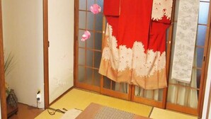 Ein traditioneller japanischer Raum mit Tatami-Bodenbelag, einem niedrigen Tisch mit einer gewobenen Matte und Schiebetüren mit roter und weißer Dekoration.