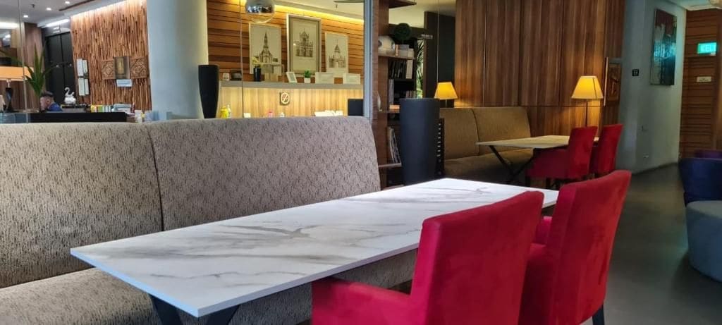 A hotel lobby with a reception desk, a seating area with a marble table, and red chairs.