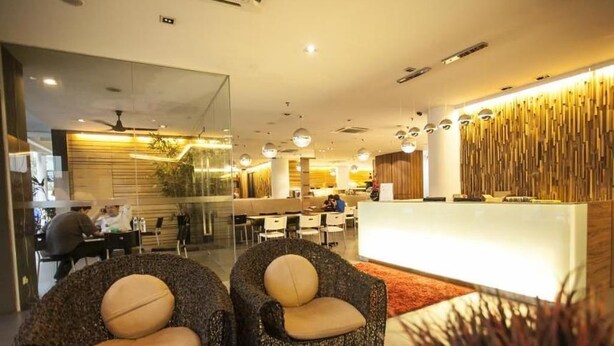 A modern hotel lobby with wicker chairs, a reception desk, and a glass partition. - Extreme Boutique Hotel (Kluang)