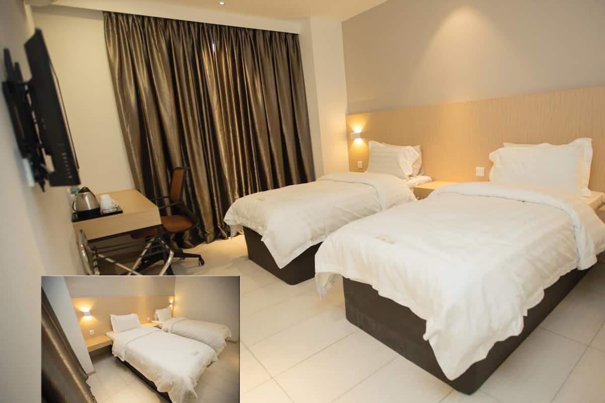 A hotel room with two beds, a desk with a chair, a TV mounted on the wall, and a window with curtains.