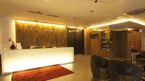 A modern reception area with a light-colored reception desk, a red rug, and two dark-colored chairs. - Extreme Boutique Hotel (Kluang)